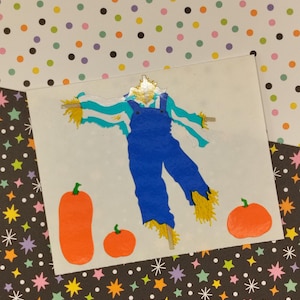 May include: A colorful sticker featuring a scarecrow with blue overalls and a straw hat. The scarecrow is standing in front of three orange pumpkins.