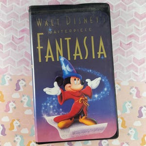 Può includere: Una videocassetta VHS di Fantasia di Walt Disney. La copertina presenta Topolino in abito da mago, con il titolo in lettere dorate. Lo sfondo è blu scuro con stelle ed effetti magici. La cassetta è su uno sfondo rosa.