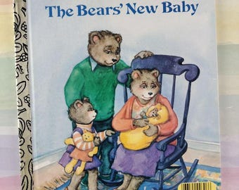 May include: A Little Golden Book titled The Bears' New Baby, featuring an illustration of three anthropomorphic bears. One bear sits in a blue rocking chair holding a baby bear in a yellow blanket, while another bear stands nearby.