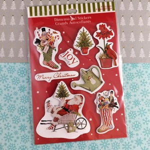 May include: A package of dimensional Christmas stickers on a red background. The stickers include images of a Christmas tree, Santa Claus, a cardinal, and a watering can. The words "Merry Christmas" and "Joy" are also included.