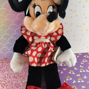 May include: A plush Minnie Mouse doll with a cream-colored bow, black ears, and a red and white polka-dot dress. The doll has black pants, white gloves, and red shoes. The tag reads "applause".