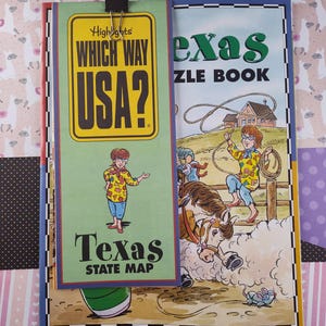 Puede incluir: Un libro verde y amarillo con el título "Which Way USA?" y el texto "Texas State Map" en la portada. El libro está unido a un libro más grande con el título "Texas Puzzle Book" y una ilustración de una niña montando a caballo.