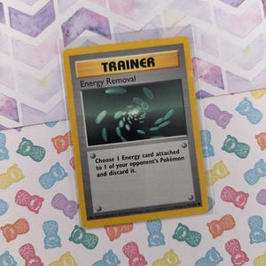 May include: A yellow Pokemon trading card with the text "TRAINER" and "Energy Removal". The card features an illustration of a swirling pattern of green energy cards.