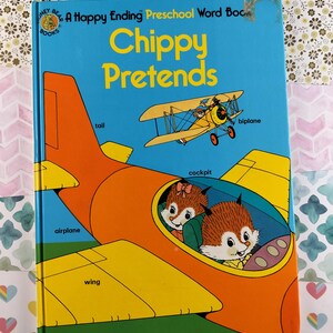 May include: A blue book with the title "Chippy Pretends" and a picture of two chipmunks in a yellow and orange airplane. The words "airplane", "wing", "tail", "cockpit", and "biplane" are labeled on the image.