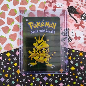 May include: A green and yellow Pokemon trading card featuring a yellow and black striped Pokemon with a spiky head. The card has the text "Pokemon" and "Gotta catch 'em all!" on it.