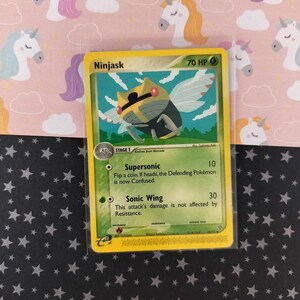 Pode incluir: Um cartão de troca Pokémon Ninjask com uma borda amarela. O cartão apresenta uma ilustração de uma criatura semelhante a um inseto com asas. O texto do cartão inclui as habilidades "Supersonic" e "Sonic Wing".