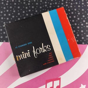 May include: A vintage box of 12 stainless steel mini forks. The black box has a white, blue, and red striped design on the side. Text on the box reads "mini forks" and "for fruit, cheese, canapes, hors d'oeuvres."