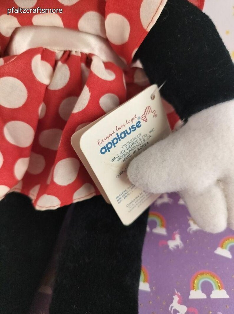 May include: A plush doll featuring a red dress with white polka dots. The doll has black legs and arms, a white glove, and a tag that reads "Everyone loves to get applause". The doll is a collectible item.