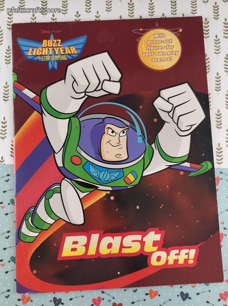Peut inclure: Couverture de livre Buzz Lightyear avec le titre "Buzz Lightyear of Star Command" et les mots "Blast Off!" en jaune et rouge. L'image pr&eacute;sente Buzz Lightyear dans une combinaison spatiale verte et blanche, les bras lev&eacute;s en poing. La couverture dit aussi "Avec des figurines &agrave; d&eacute;couper pour vos propres sc&egrave;nes de jeu!"