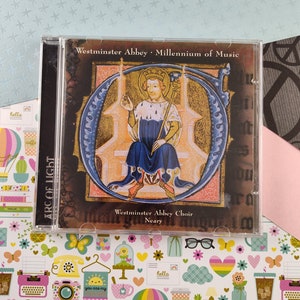 Peut inclure: Un boîtier de CD avec une image colorée d'un roi assis sur un trône. Le texte sur le boîtier indique "Westminster Abbey Millennium of Music" et "Westminster Abbey Choir Neary".