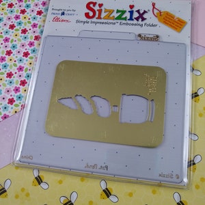 Può includere: Una cartella di goffratura in metallo dorato con un design di un barattolo e tre foglie. La cartella è confezionata in una custodia di plastica trasparente con il nome del marchio "Sizzix" e il testo "Simple Impressions™ Embossing Folder".