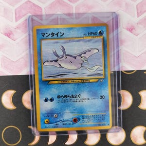 May include: A Pokemon trading card featuring a Manta Ray illustration in a protective sleeve. The card has Japanese text and a blue and white color scheme. The card is on a background with a crescent moon pattern.
