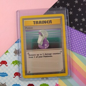 May include: A Pokemon trading card featuring a purple potion bottle with the text "Potion" and "Trainer" on the card. The card also has the text "Remove up to 2 damage counters from 1 of your Pokemon."