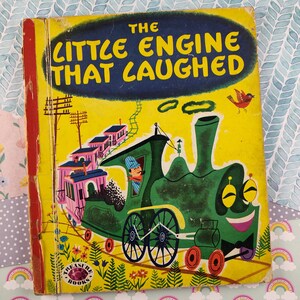 Może przedstawiać: Antyczna książka dla dzieci zatytułowana "The Little Engine That Laughed" z zielonym lokomotywa na okładce. Lokomotywa ma uśmiechniętą twarz i ciągnie różowy wagon pasażerski. Książka jest częścią serii "Treasure Books".