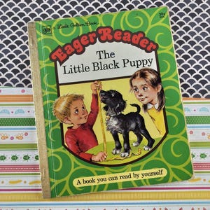 May include: A vintage children's book titled "Eager Reader The Little Black Puppy." The cover is green with illustrations of a boy, girl, and a black puppy. The book has a gold spine and the text "A book you can read by yourself."