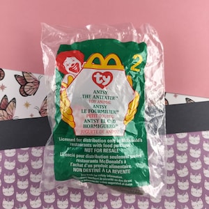 May include: A clear plastic bag containing a Ty Beanie Baby plush toy named "Antsy the Anteater". The bag is green and yellow with the McDonald's logo and the text "Licensed for distribution only by McDonald's restaurants with food purchase. Not for resale."