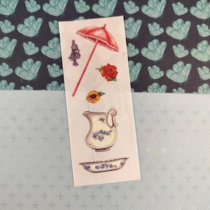 Peut inclure: Une planche d'autocollants avec diverses illustrations de style vintage. La planche comprend un parasol rouge, une rose rouge, une fleur jaune, un ensemble pichet et bassin avec des détails floraux bleus et un objet décoratif. Le fond est un motif bleu et blanc.