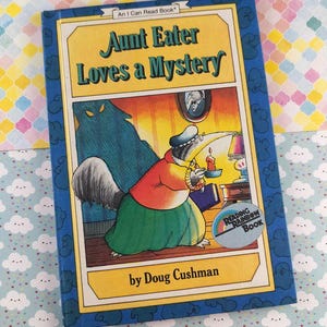 May include: A children's book titled "Aunt Eater Loves a Mystery" by Doug Cushman. The cover features an illustration of an anteater holding a candle, with a shadowy figure in the background. The book is part of the "An I Can Read Book" series.
