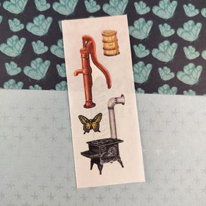 Peut inclure: Une planche d'autocollants avec des illustrations de style vintage. Elle comprend une pompe à eau rouge, un petit baril en bois, un papillon jaune et noir et un poêle noir avec une cheminée. Le fond présente un motif de papillons bleus.