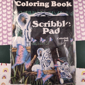 Puede incluir: Un conjunto de libro para colorear con un cachorro de tigre blanco y mariposas. El conjunto incluye un libro para colorear, una libreta para garabatear y lápices de colores. El embalaje es de plástico transparente y muestra el contenido del conjunto.