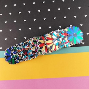 Peut inclure: Une collection d'ornements en forme de fleurs colorées. Chaque fleur présente un design unique avec un mélange de couleurs, dont le bleu, le rouge, le jaune et le vert. Le fond est noir avec des cœurs blancs et des rayures jaunes et roses en bas.