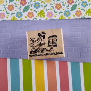May include: A wooden stamp with a cartoon illustration of a person holding a piece of pie and the text "Now you've had fractions".