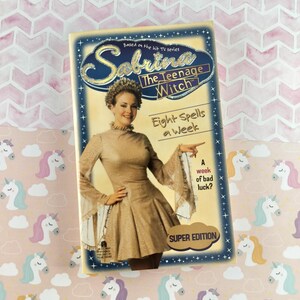 May include: A book cover for "Sabrina the Teenage Witch: Eight Spells a Week." The cover features a woman in a gold dress, with the title in gold lettering. The book is a "Super Edition."