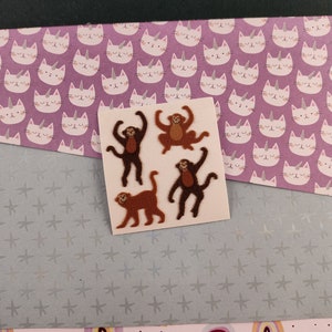 May include: Four brown monkey stickers on a white sheet of paper. The monkeys are in different poses, including standing, sitting, and swinging. The stickers are ideal for adding a touch of whimsy to any project.