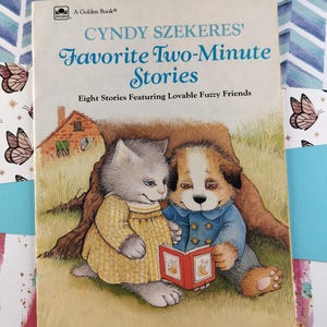 May include: A Golden Book children's book titled "Cindy Szekere's Favorite Two-Minute Stories" featuring a cat and dog reading a book together. The book cover is illustrated with a yellow house, green grass, and a tree.