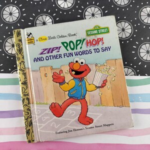 Puede incluir: Un libro infantil vintage titulado "ZIP! POP! HOP! AND OTHER FUN WORDS TO SAY" con Elmo de Barrio Sésamo. La portada muestra a Elmo sosteniendo palomitas de maíz. El libro es un "First Little Golden Book."