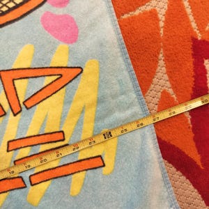 May include: A light blue beach towel with a tennis racket design and abstract shapes in orange, yellow, and pink. The towel measures approximately 29 inches in length.