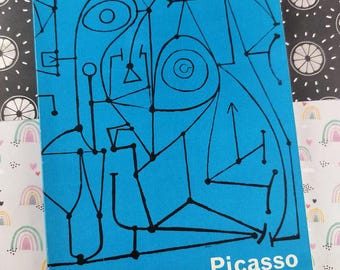 May include: A blue book cover featuring a black line drawing in an abstract style. The word "Picasso" is printed in white, with "The Arts Council of Great Britain 1960" below. The background is patterned with black and white circles and rainbows.