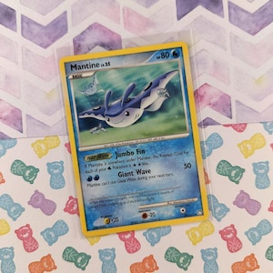 May include: A Mantine lv.25 Pokémon trading card in a protective sleeve. The card features a blue and white aquatic creature illustration with the text "Mantine" and "Giant Wave". The card is on a patterned background.