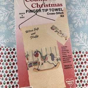 以下が含まれることがあります： カントリークリスマス指先タオルクロスステッチキット。キットには、壁掛け、針、糸、説明書が含まれています。デザインはロッキングホースと電車が特徴です。パッケージには「Ultra Soft and Fluffy」と書かれています。