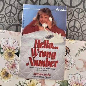 Puede incluir: Un libro de bolsillo titulado "Hello... Wrong Number" de Marilyn Sachs. La portada presenta a una mujer sosteniendo un teléfono blanco. El título es en rojo, con la leyenda "It turned out to be the best mistake she ever made!"