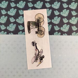 Peut inclure: Un autocollant rectangulaire avec deux illustrations de véhicules anciens. L'illustration supérieure représente une voiture ancienne noire et grise avec de grandes roues à rayons. L'illustration inférieure montre un biplan gris avec un emblème rouge et blanc.