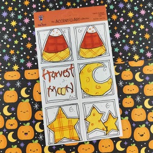 May include: A sheet of Halloween-themed stickers featuring candy corn, a crescent moon, and stars. The text "Harvest Moon" is handwritten. The background is patterned with pumpkins, moons, and stars.