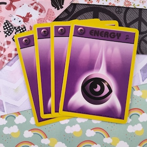 May include: Four purple Pokemon Energy cards with a yellow border and a single eye symbol in the center. The text "ENERGY" is printed in black at the top of the card.