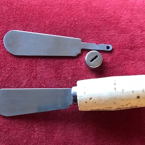 May include: Two stainless steel butter knives with cork handles. One knife has a cork handle and the other has a metal handle with a small hole.