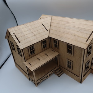 May include: A wooden model of a two-story house with a porch and steps. The house is made of light brown wood and has a simple design.