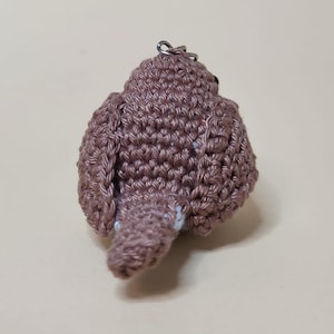 May include: A handmade, crocheted bird keychain in shades of brown. The bird has a rounded body, wings, and a small tail. A silver-colored metal ring is attached to the top for hanging. The bird is made with a textured stitch.