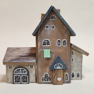 May include: A wooden miniature house with a brown and gray exterior, a green cloth hanging on a clothesline, and a white heart on the door.