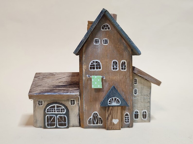 May include: A wooden miniature house with a brown and gray exterior, a green cloth hanging on a clothesline, and a white heart on the door.