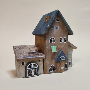 May include: A miniature wooden house with a gray roof, brown siding, and white trim. The house has a small porch with a heart-shaped door and a green and white checkered cloth hanging from a line.