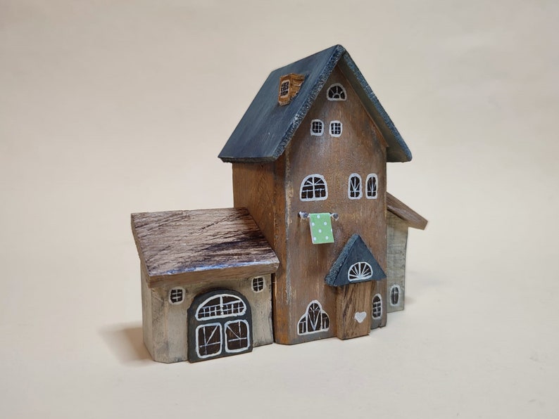 May include: A miniature wooden house with a gray roof, brown siding, and white trim. The house has a small porch with a heart-shaped door and a green and white checkered cloth hanging from a line.