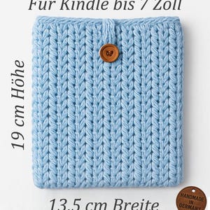 May include: A light blue knitted Kindle cover with a wooden button closure. The cover is 19 cm high and 13.5 cm wide, designed to fit Kindles up to 7 inches. The tag reads "Handmade in Germany".