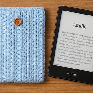 May include: A light blue knitted Kindle cover with a wooden button closure next to a black Kindle e-reader. The Kindle displays the word "kindle" and text on its screen. The cover is made of a thick, textured yarn.