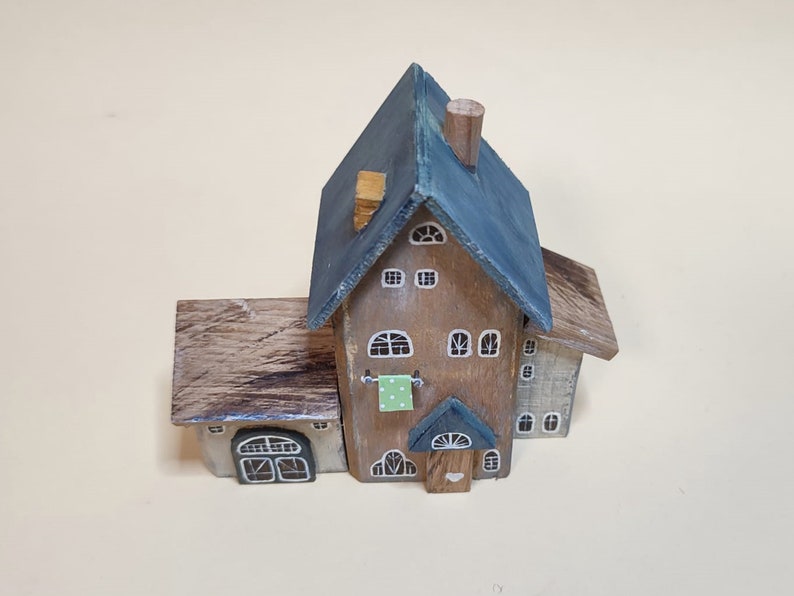 May include: A miniature wooden house with a blue roof, brown siding, and white windows. The house has a small porch with a green door and a white heart.