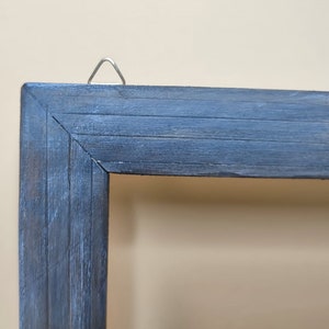 May include: A close-up of the top corner of a dark blue wooden picture frame. The frame has a distressed finish and a metal hanging hook.