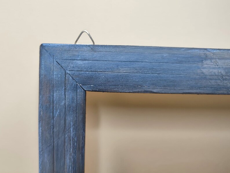 May include: A close-up of the top corner of a dark blue wooden picture frame. The frame has a distressed finish and a metal hanging hook.